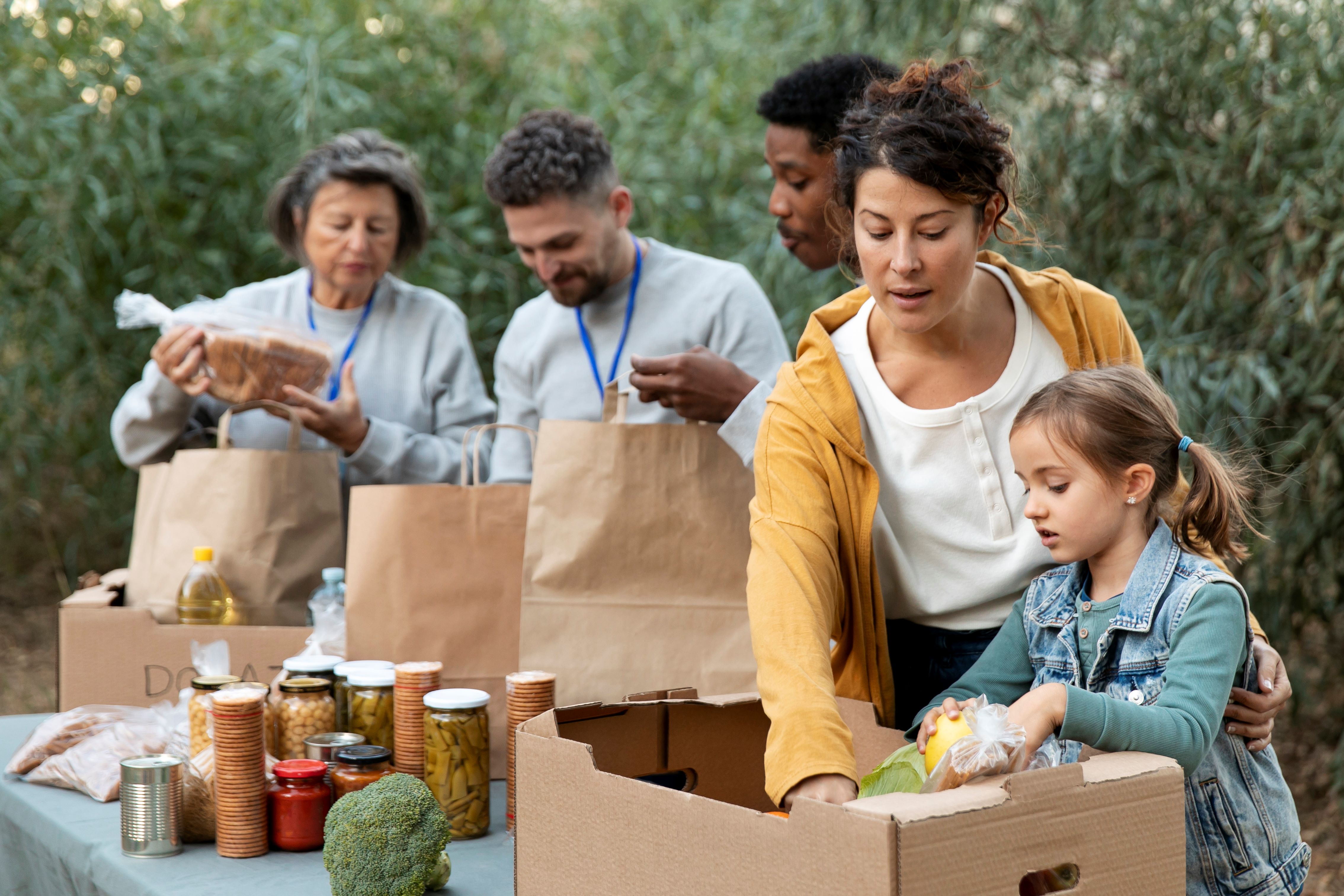Cinco pessoas verificando os alimentos recebidos. Uma das pessoas é uma criança ajudando.